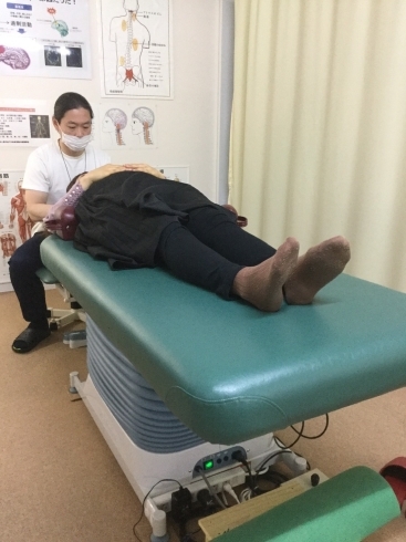 Here is a patient lying down while receiving treatment on the automatic stretcher. The chiropractor is sitting on a bench performing a maneuver on the patient's neck.